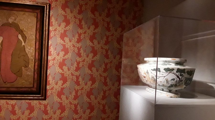 An elegant china piece spotlighted against ornately printed wallpaper.