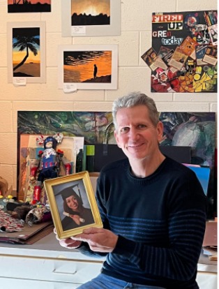 Art teacher Michael McDermott holds the high school graduation photo of Katherine, surrounded by the artwork his students produced. 

