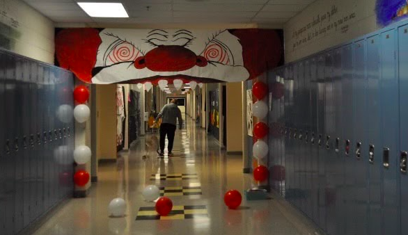 A student walks down the Juniors Haunted Carnival themed hall. A detailed clown face and red and white ballons hang on the wall.
