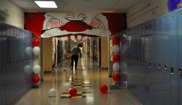 A student walks down the Junior's 'Haunted Carnival' themed hall. A detailed clown face and red and white ballons hang on the wall.