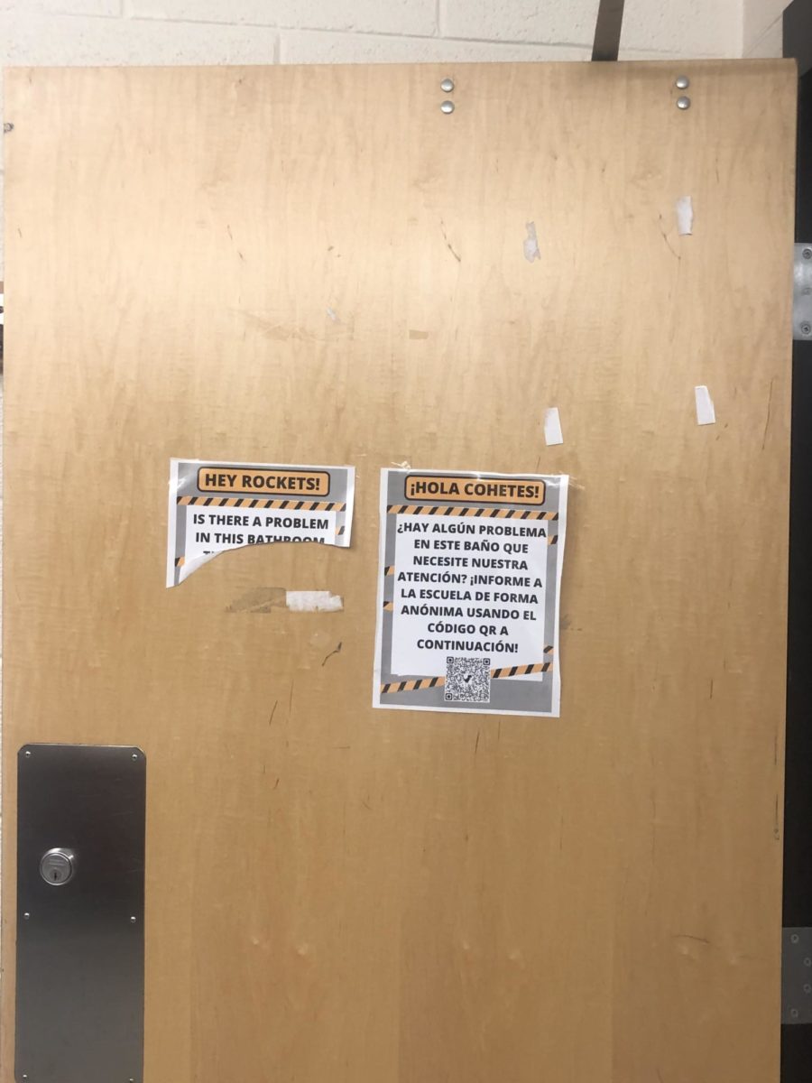 Flyers, in Spanish and English, hang on the RM boys bathroom door with a QR code for students to submit issues with the bathroom.
