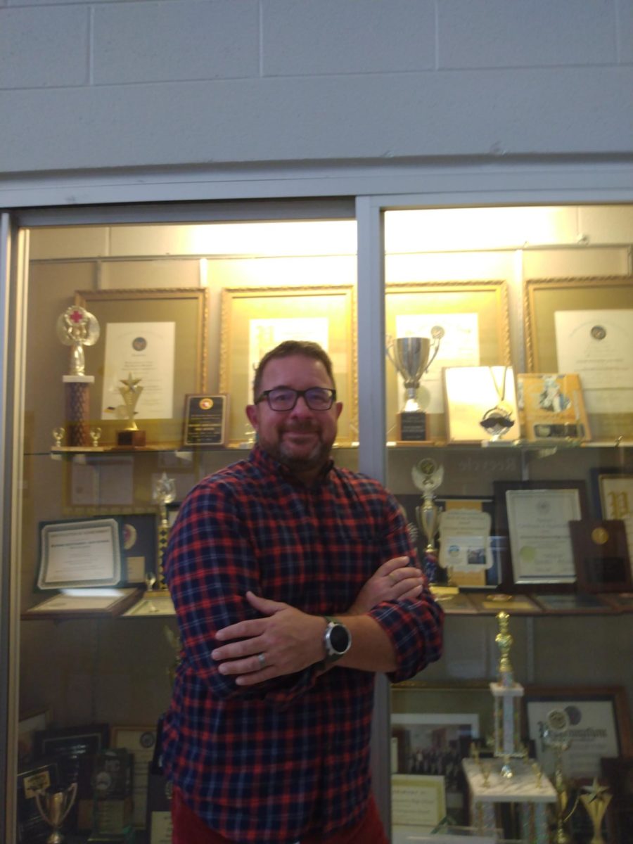 Mr. Matthew Martini, poses in front of Richard Mongtomery's trophy case, specifically a few of the lacrosse trophies that have been awarded to RM. 