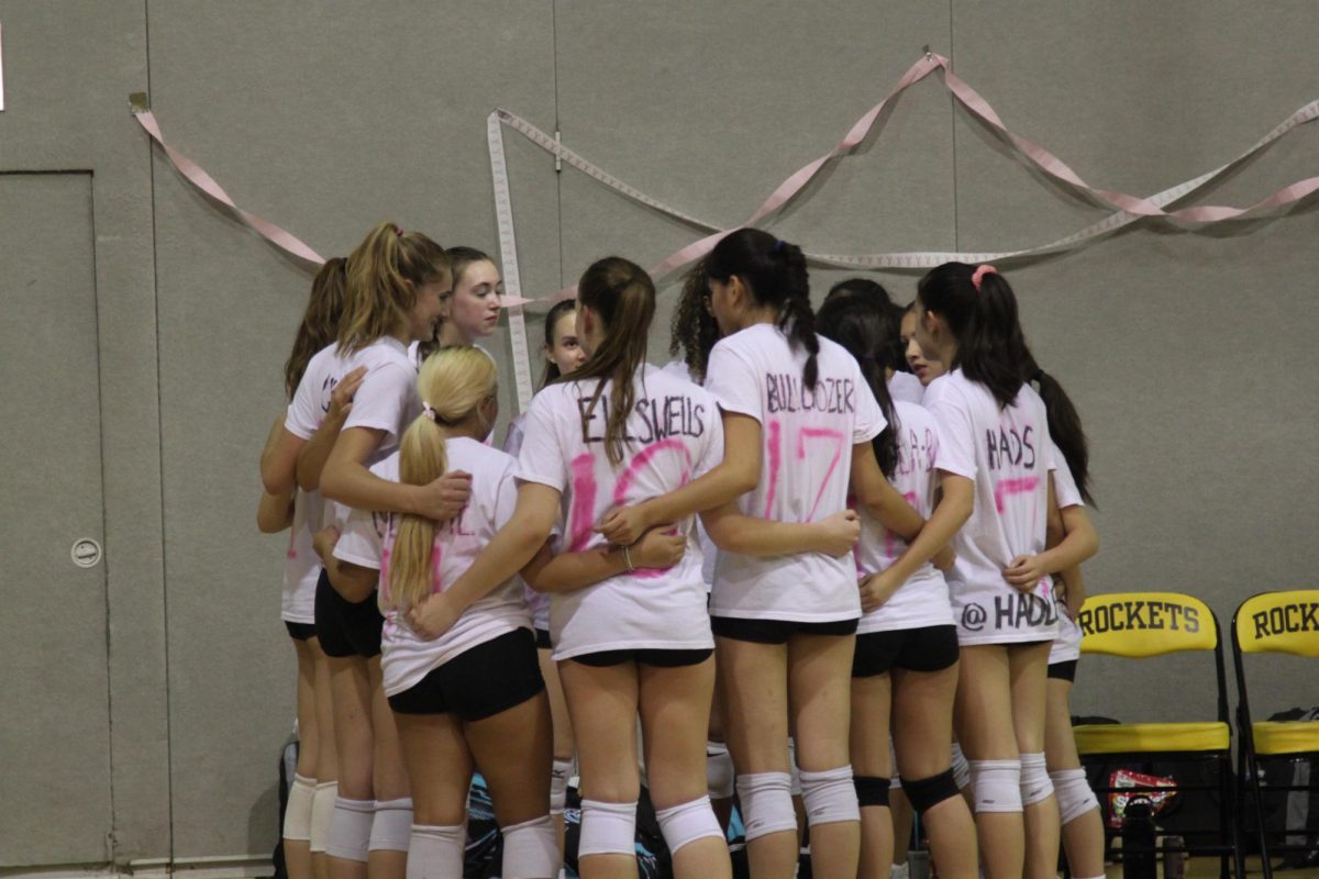 The girls varsity volleyball team gathers into a team huddle before their next set. 