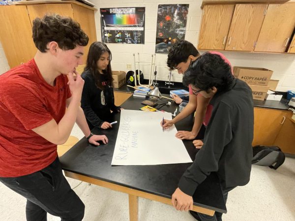 Members of RM Engineering plan out a design for their Rube Goldberg machine on a poster board.