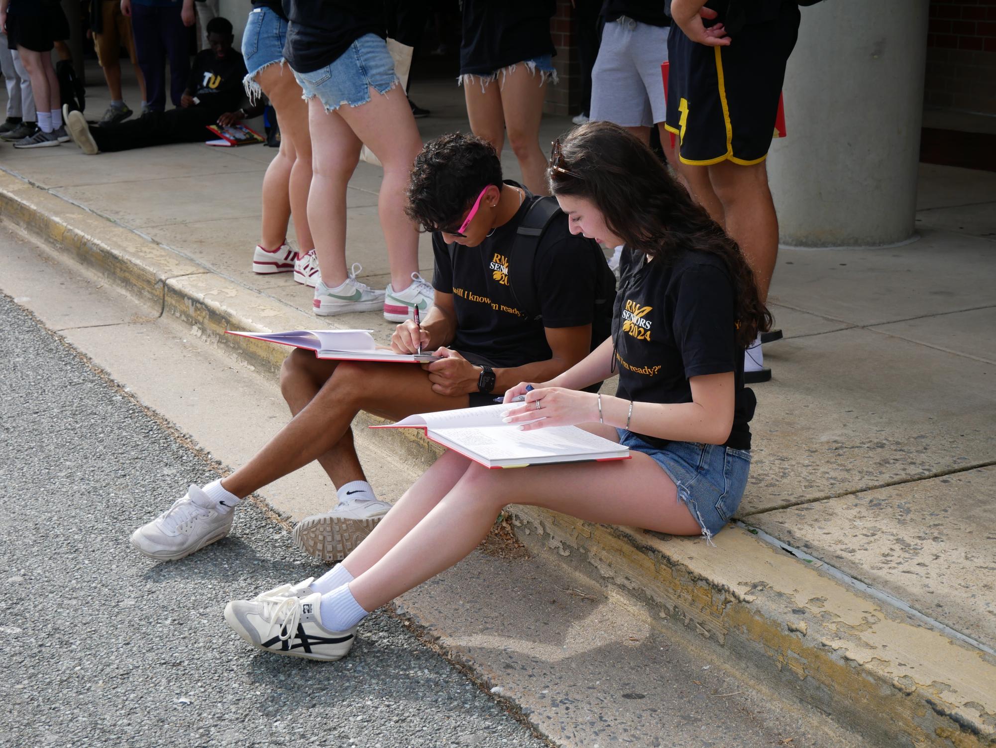 Seniors Zaki Ahmad and Arielle Schmeidler sign each others yearbooks outside of the school on their last day.