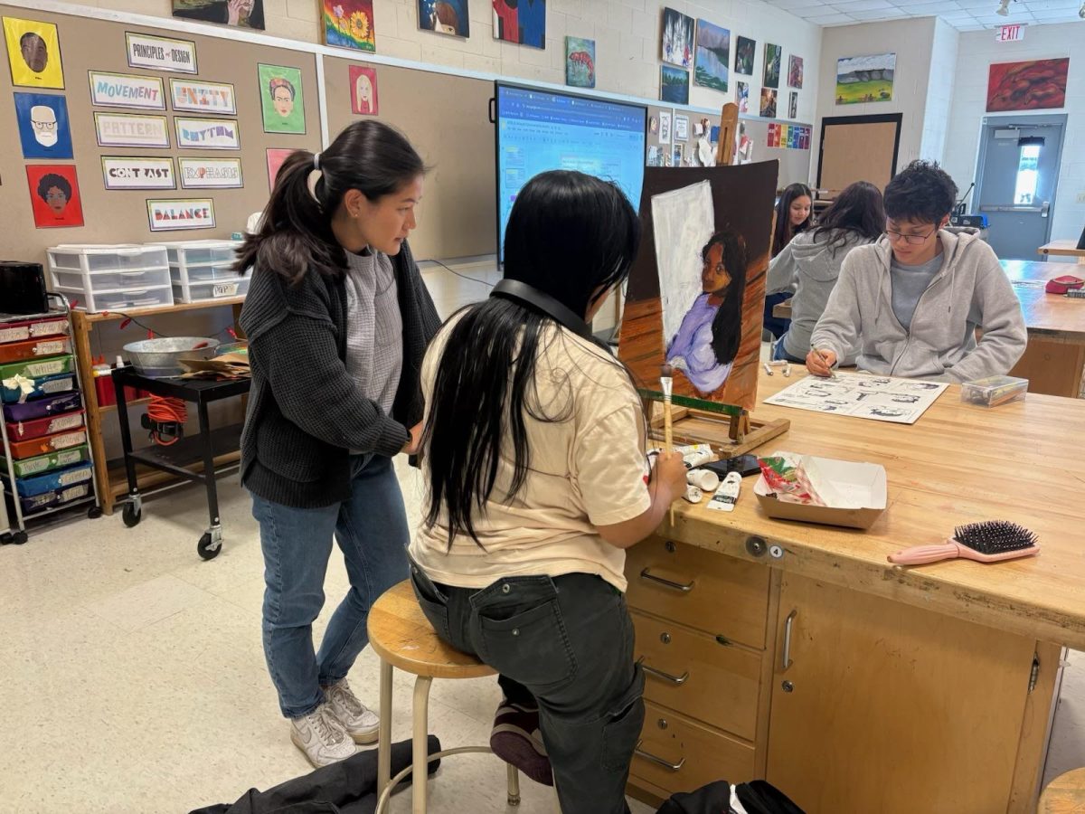 Ms. Coryell instructs a student on a painting as senior Josiah Main works on a drawing in the background.