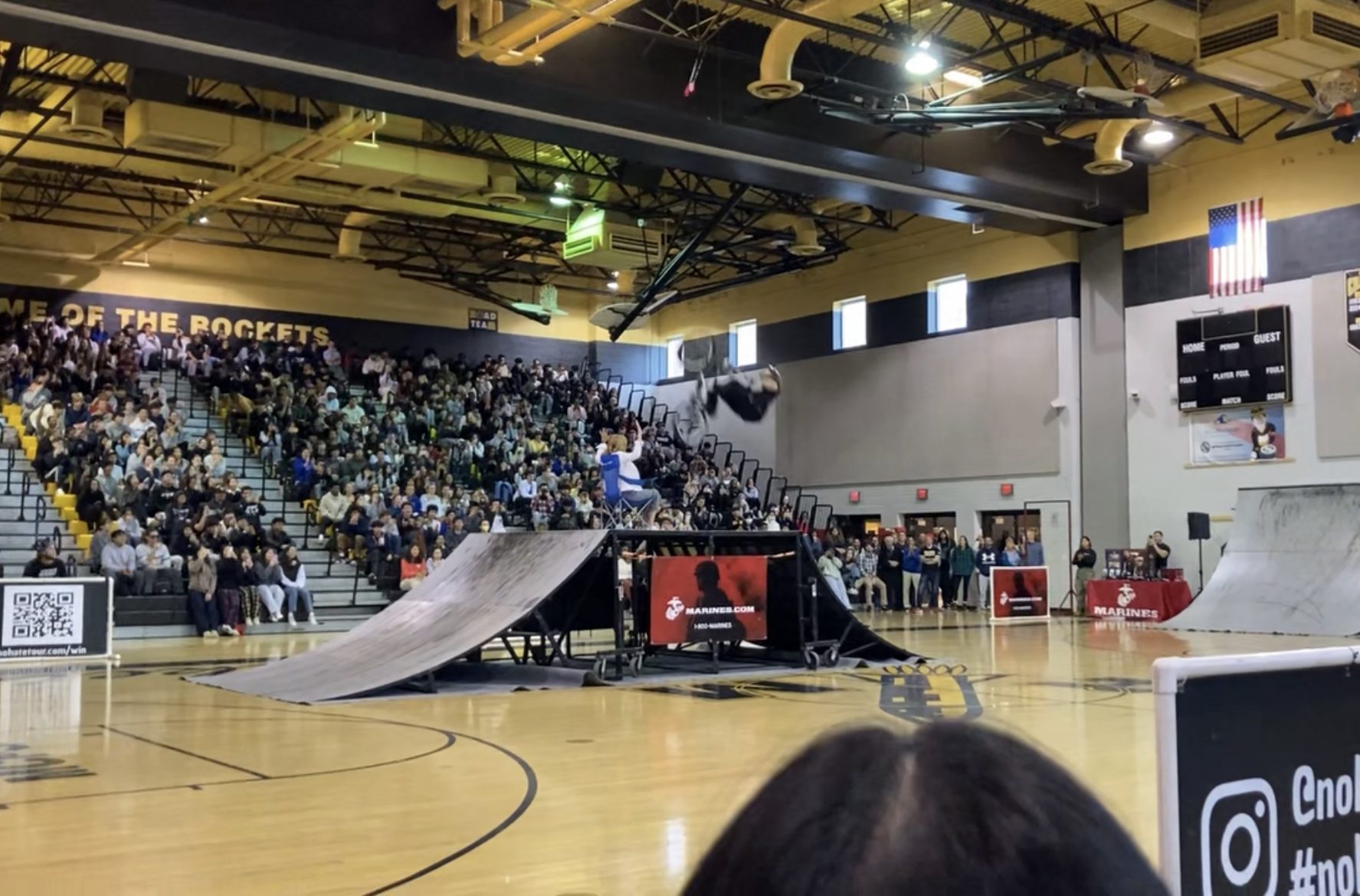 Math teacher Laura Goetz sits atop an elevated platform as a BMX rider flips over her.