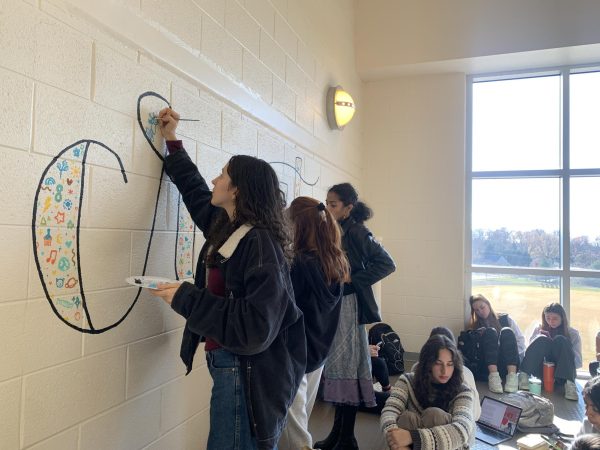 Senior Naima Aubry-Romero paints a portion of the calligraphy mural during lunch.