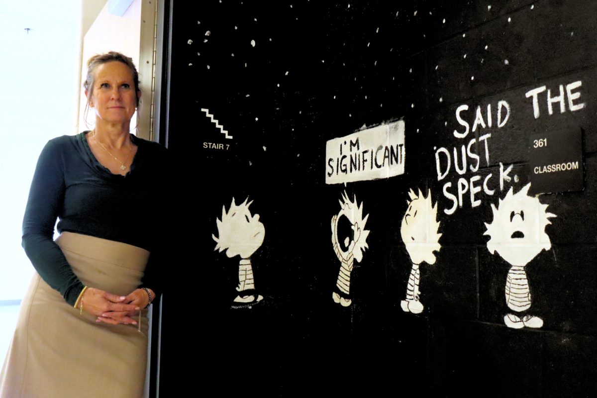 Ms. Goetz leans next to a mural. After the move to the new RM building, Mr. Goetz commissioned his students to decorate the walls in exchange for SSL hours.