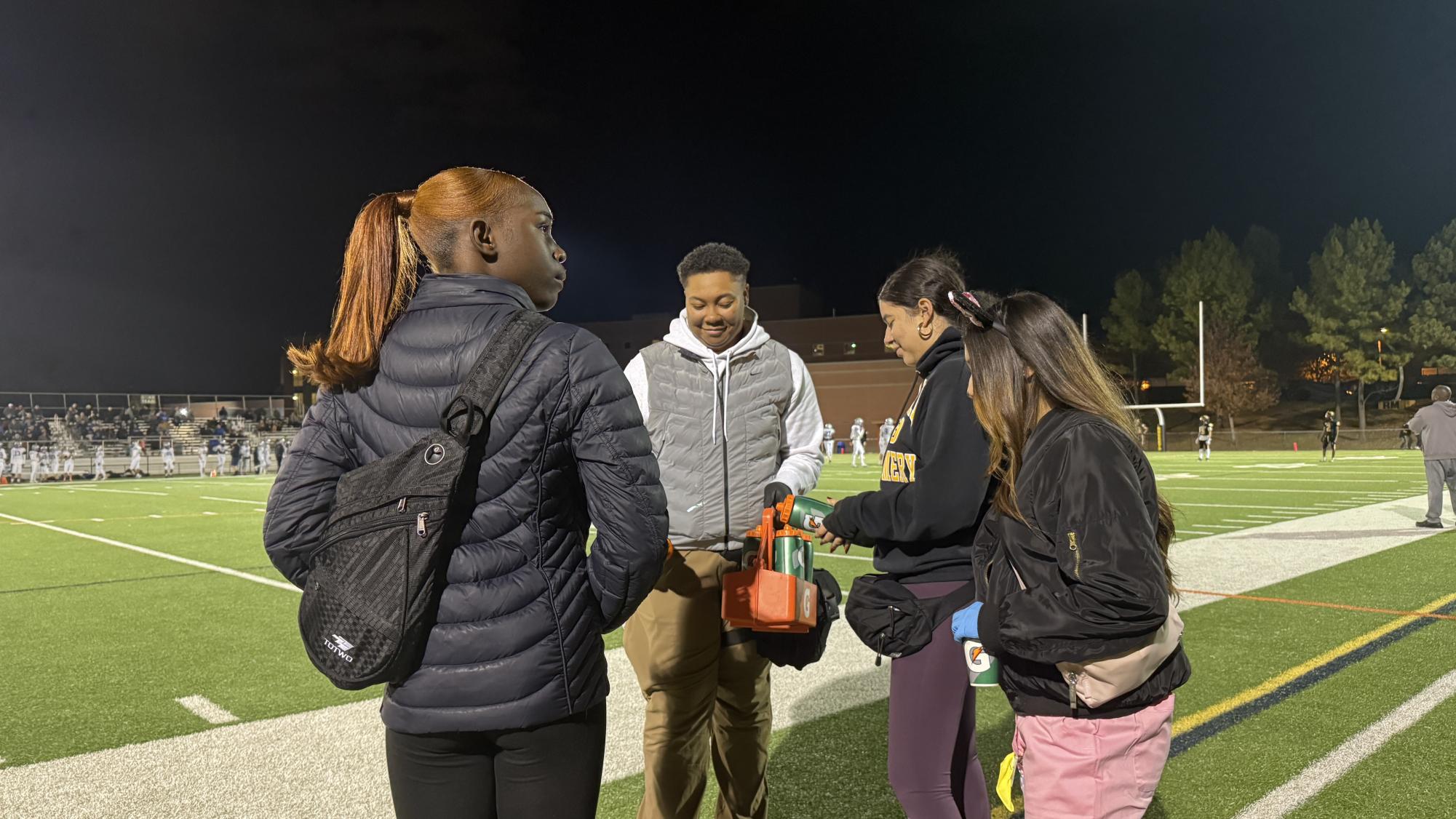 Seniors Candice Dondon and Cecila Peele fill up water bottles with head trainer Dahlia "Dee" Dyson during a football game. (Photo Courtesy of Ewina Chen)