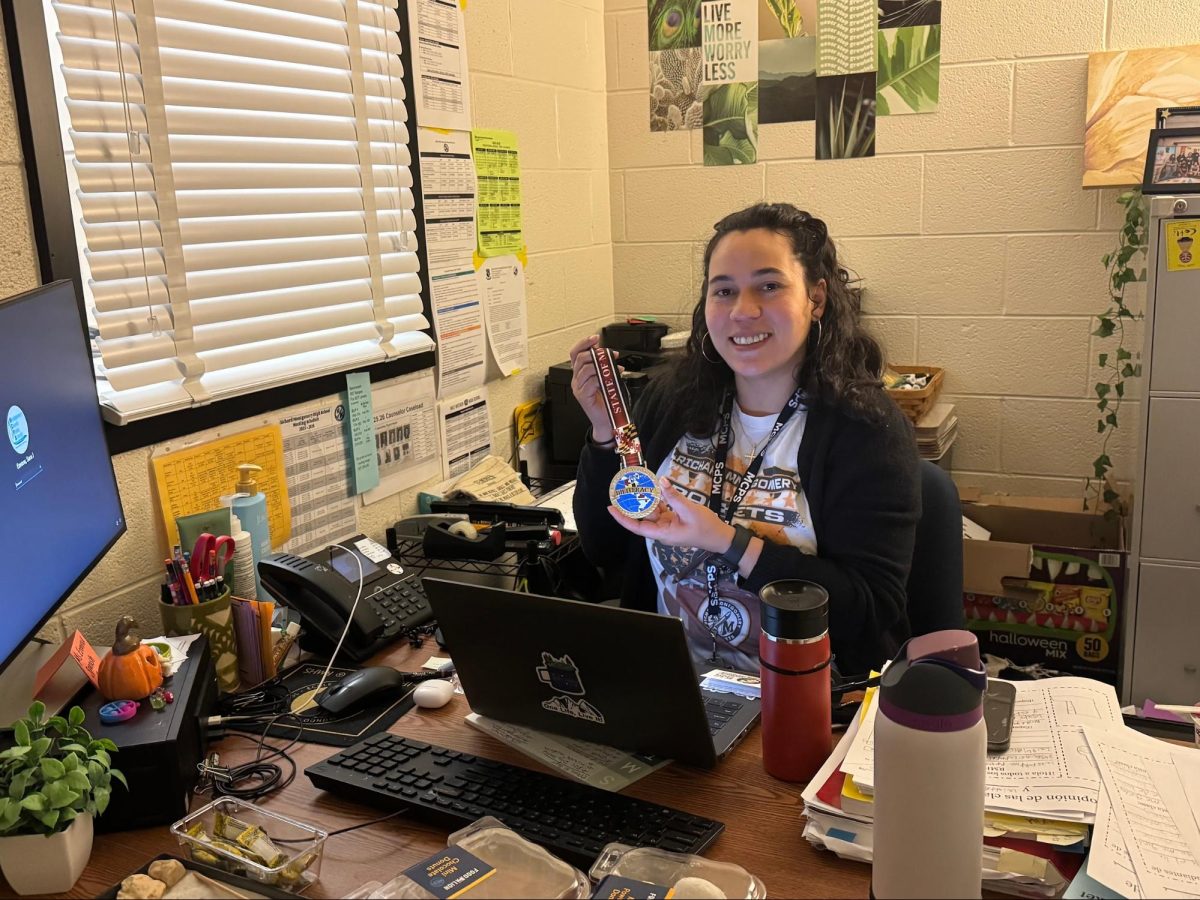 Ms. Ezeonu sits at her desk holding the Maryland Seal of Biliteracy medal.