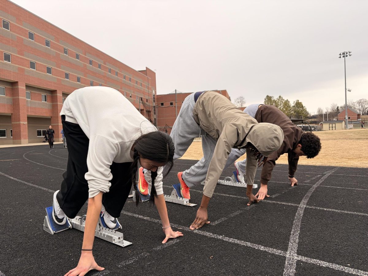 Junior Alvaro Gonzales-Ysern, junior Lydia Chao, and sophomore Jayce Bigirimana brace in their starting blocks and press their hands against the track during an after-school practice. 