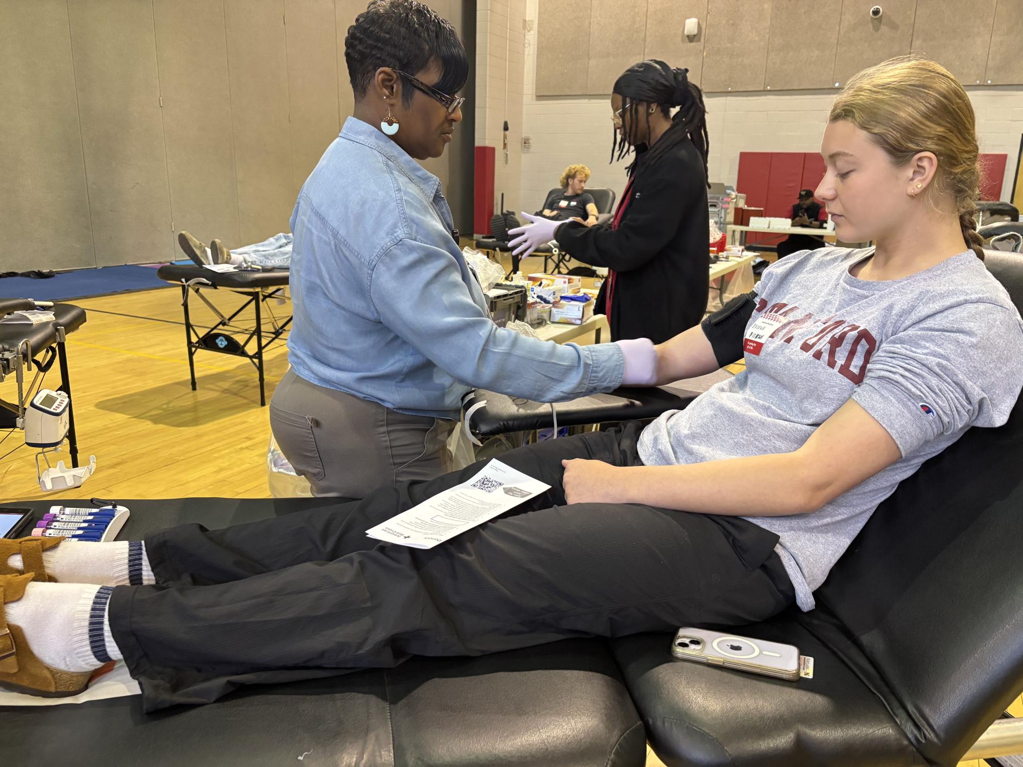 Junior Brooke Bennett watches as a volunteer cleanses her arm before drawing blood.