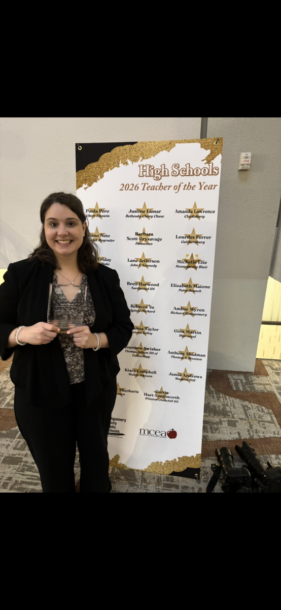 Social studies teacher Amber Myren poses with her award against the 2026 Teacher of the Year banner. (Photo courtesy of Amber Myren)