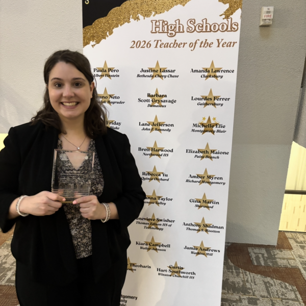 Social studies teacher Amber Myren poses with her award against the 2026 Teacher of the Year banner. (Photo courtesy of Amber Myren)